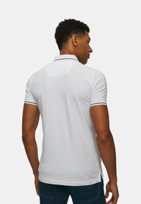 Polo bianco con colletto e maniche corte, dotato di rifiniture nere sul colletto e sulle maniche. Tessuto liscio con design slim fit.