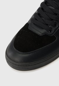 Fekete sneaker sima bőr és velúr keverékből, perforációkkal az orrán és fekete fűzőkkel. Lapos gumitalp, varrással díszítve.