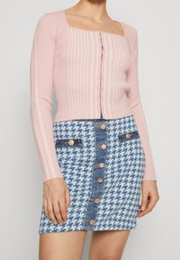 Top lungo a maniche lunghe rosa a coste con scollatura quadrata, abbinato a una gonna di jeans a quadri blu e bianca con dettagli in bottoni dorati.