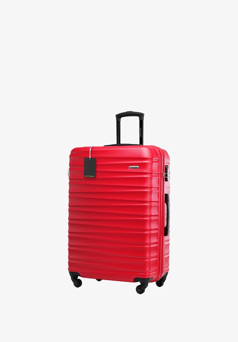 Maleta roja de concha dura con un diseño estriado, mango retráctil negro, ruedas para movilidad y una etiqueta adjunta.