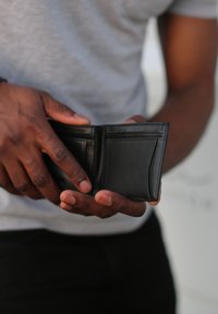 Black leather wallet held in hands, featuring multiple card slots and a sleek design. The surface appears smooth with subtle stitching details.