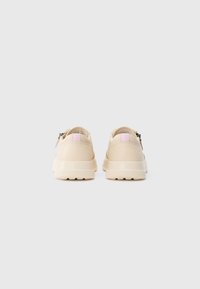 Pair of beige sneakers with chunky soles and pink pull tabs seen from the back on a plain white background.