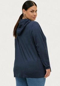 Sudadera de color azul marino con una textura suave, mangas largas y un corte relajado. Presenta un diseño en la parte posterior con capucha para mayor comodidad.
