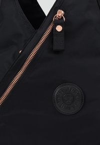 Zwarte tas van gladde stof met een koperkleurige ritssluiting, zwart logo-patch en een gestructureerde trekband voor gemakkelijke toegang.