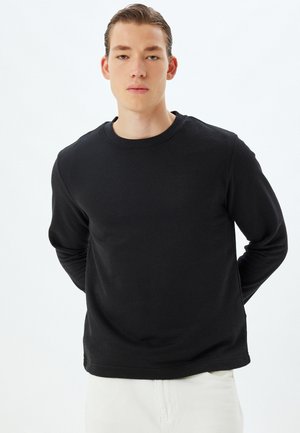 Zwarte trui met lange mouwen, met een geribbelde textuur en een ronde hals. Heeft een relaxte pasvorm en een eenvoudig ontwerp, geschikt voor casual kleding.