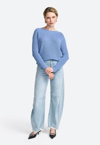 Helles blaues Strickpullover mit langen Ärmeln, kombiniert mit hellen, weit geschnittenen Jeans und schwarzen spitz zulaufenden High Heels. Einfaches Design, lässige Passform.