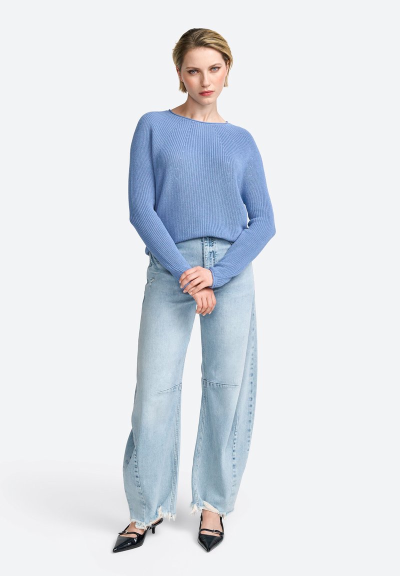 Helles blaues Strickpullover mit langen Ärmeln, kombiniert mit hellen, weit geschnittenen Jeans und schwarzen spitz zulaufenden High Heels. Einfaches Design, lässige Passform.