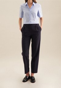 Ljusblå kortärmad skjorta med knappar, tillsammans med mörkblå högmidjade byxor och svarta loafers. Slät textur, skräddarsydd passform.