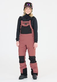 Skiausrüstung in Dunkelpink und Schwarz; verfügt über verstellbare Träger, mehrere Taschen und eine strukturierte Oberfläche. Enthält Skischuhe und eine Skibrille.