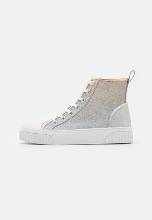 Sneaker wysokiego typu z białą gumową podeszwą, błyszczącą srebrną tkaniną, białymi sznurówkami oraz złotymi wykończeniami na jednolitym jasnym tle.