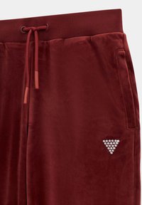 Czerwone welurowe dresy z miękką teksturą, elastycznym pasem, zapięciem na sznurek oraz detalem w postaci logo w kształcie trójkąta ozdobionego cyrkoniami na boku.