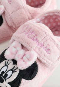 Pink plush slippers feature a black embroidered Minnie Mouse face, a pink bow with white polka dots, and a soft fabric lining.