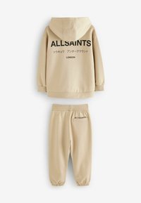Beżowa bluza z kapturem z czarnym logo "ALLSAINTS" na plecach, zestawiona z dopasowanymi spodniami dresowymi z detalem logo i elastycznymi mankietami.