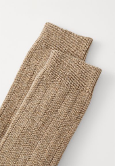Beige gerippte Socken mit einem strukturierten Strickmuster und umgeschlagenem Bündchen. Das Material sieht warm und gemütlich aus.