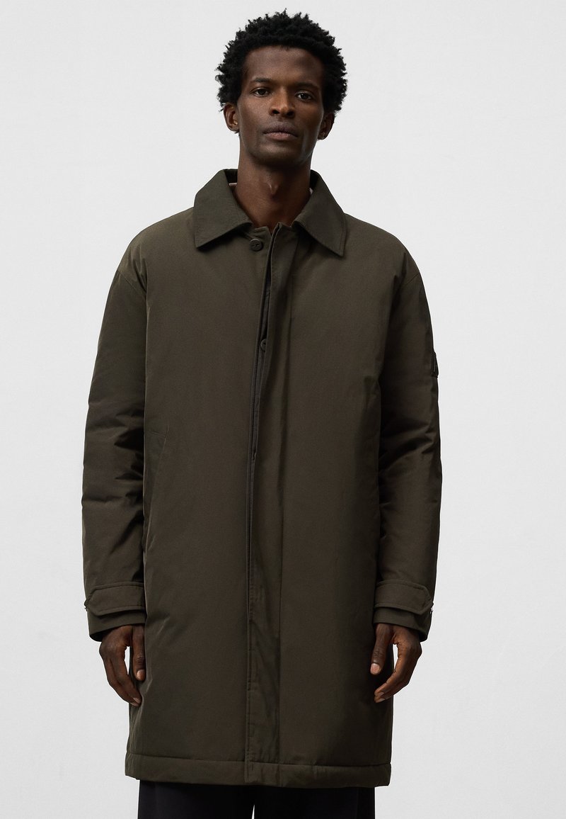 Cappotto lungo verde oliva con chiusura a bottoni, grande colletto e tasche laterali; presenta una texture liscia e imbottita con una vestibilità su misura.