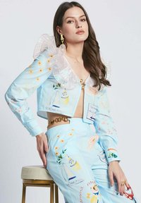 Short, light blue cropped jacket with transparent ruffled collar; embroidered floral patterns and artistic graphics. Gold hardware accent on pants.