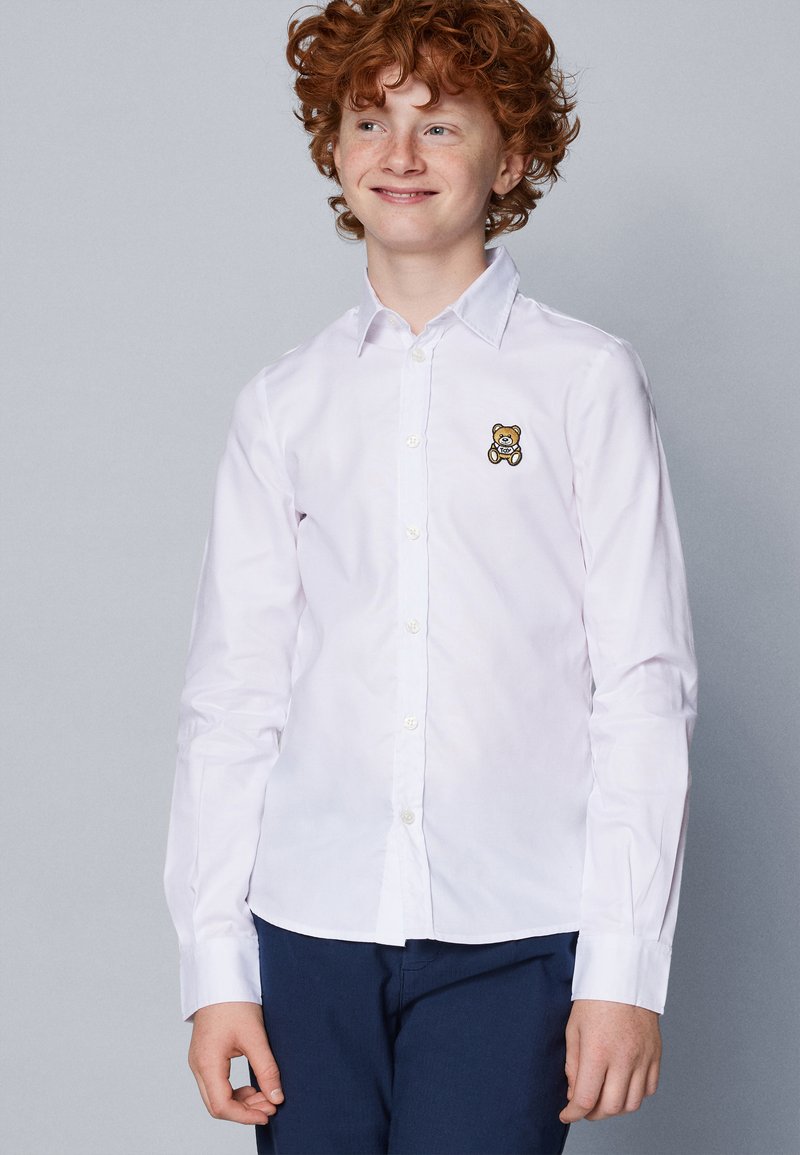 Camicia bianca a maniche lunghe con chiusura a bottoni, caratterizzata da un piccolo orsetto ricamato sul lato sinistro del petto. Tessuto liscio, vestibilità slim.