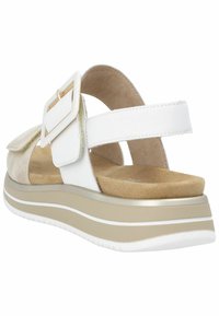 Valkoinen ja beige sandaali, jossa on säädettävät hihnat, paksu pohja ja kultaiset yksityiskohdat. Pehmeä mokka ja sileät materiaalit käytetty.