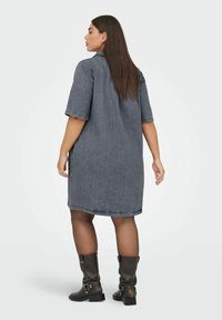 Jeansklänning med korta ärmar, mörkblå tvätt, knälång skärning, något lös passform, tillsammans med knähöga svarta stövlar med spännen.