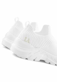 White slip-on sneakers with a textured, ribbed fabric upper and a chunky white sole. Features a subtle logo on the heel.