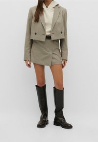 Cropped plaid blazer with two buttons, paired with a beige hoodie and a checkered mini skirt. Black knee-high boots with a chunky sole.