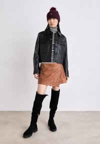Veste en cuir noire courte, col roulé rayé, mini-jupe marron et bottes noires en daim à hauteur de genoux avec des zips. Bonnet en tricot bordeaux avec pompon.