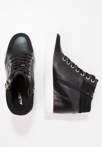 Black high-top sneakers with textured leather and suede accents, featuring metal eyelets, zippers, and a white rubber sole.