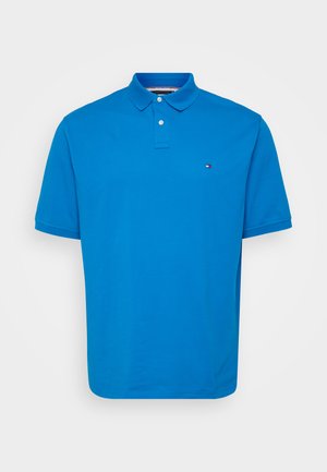 Tricou polo albastru din bumbac, cu guler clasic, fantecă cu două nasturi și un logo mic pe piept. Mâneci scurte.