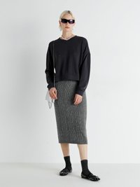 Hanorac scurt negru cu embellishe, fustă midi texturată gri, șosete închise la culoare și pantofi plati cu ținte. Accesoriile includ ochelari de soare și un colier.