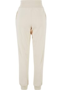 Pantalones de chándal beige con cintura acanalada, bolsillos laterales y puños acanalados; hechos de una tela suave y lisa con un corte relajado.