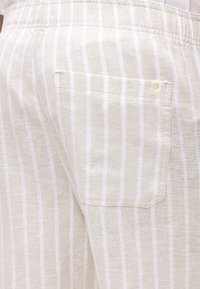 Μπεζ και λευκό υφασμάτινο παντελόνι με κάθετες ρίγες, με πίσω τσέπη που έχει μια μικρή μπεζ ετικέτα στην επάνω δεξιά γωνία.