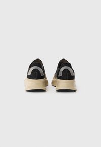 Black mesh sneakers featuring beige soles, textured detail on the upper, and contrasting grey accents on the heel and side.