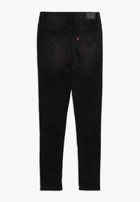 Jeans pitillo negros hechos de mezclilla, con un diseño clásico, cinco bolsillos y una etiqueta roja de Levi's en el bolsillo trasero.