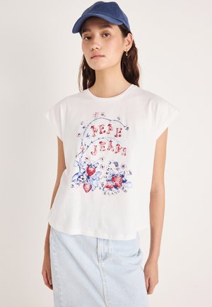 Fehér rövid ujjú póló virágmintával, piros eperrel és kék részletekkel. Világos farmer szoknyával és kék sapkával párosítva.