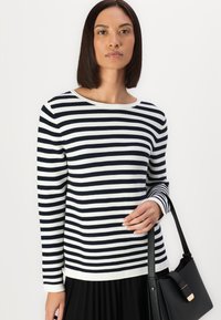 Gestreifter Pullover in Schwarz und Weiß, mit Rundhalsausschnitt und langen Ärmeln, kombiniert mit einer schwarzen Handtasche. Glattes Material und taillierte Passform.