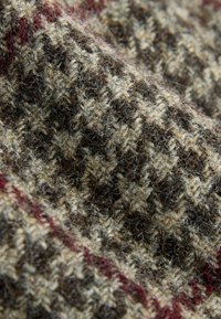 Teksturowana tkanina w brązowo-beżowy wzór w kratę houndstooth, z subtelną bordową paskiem akcentującym. Miękki, przypominający wełnę materiał.