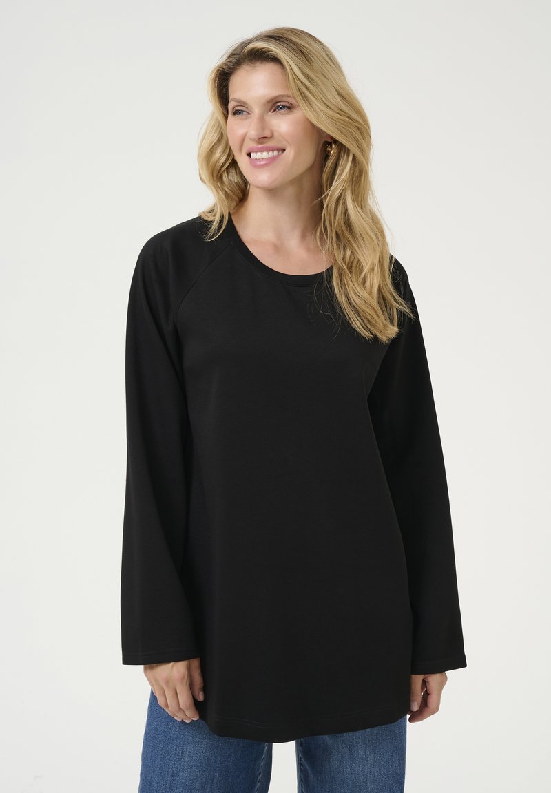 Tunic neagră, cu mânecă lungă, fabricată dintr-un material moale. Dispune de un guler rotund și mâneci raglan. Asortată cu blugi din denim albastru.