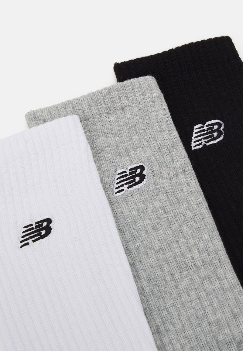 Trois paires de chaussettes côtelées en blanc, gris et noir, chacune présentant un petit logo brodé en blanc sur le haut.