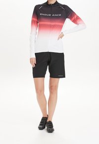 Cyklistický dres s dlouhým rukávem s přechodem z černé do bílé s červenými akcenty, doplněný černými kraťasy a černými cyklistickými botami.