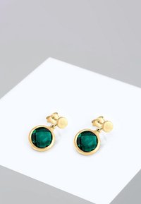 Goldfarbene Ohrringe mit großen, facettierten smaragdgrünen Glassteinen, die in runden Rahmen eingefasst sind. Glatte Oberfläche mit glänzendem Finish.