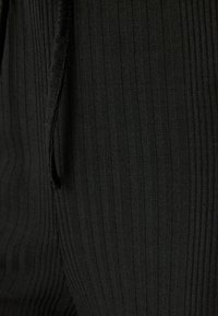 Zwarte ribstof met verticale strepen, een gestructureerd oppervlak en een trekkoorddetail, dat de vorm en pasvorm benadrukt.