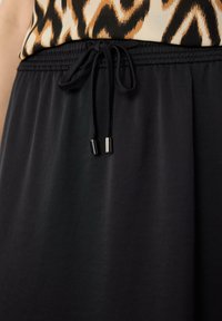 Zwarte, gladde stoffen rok met een elastische tailleband, trekkoord en metallic accenten. Heeft een vloeiende design, geschikt voor casual kleding.