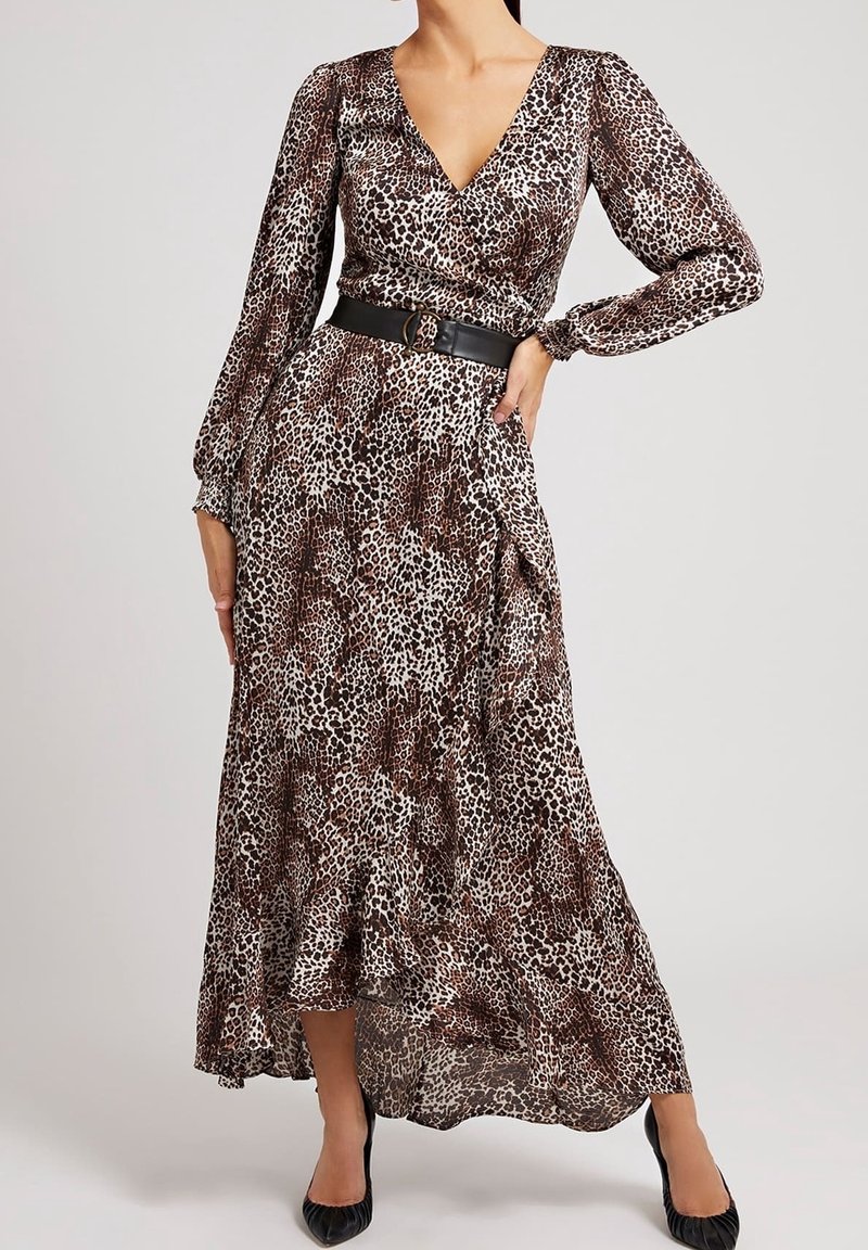 Femme portant une robe à manches longues, col en V, imprimé léopard, avec une ceinture noire et des escarpins noirs à bout pointu, posant avec une main sur la hanche.