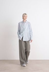 Camisa de botones azul claro con un ajuste relajado, combinada con pantalones grises holgados. El conjunto presenta un diseño mínimo y texturas sutiles.