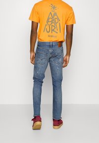 Orange t-shirt med ett grafiskt tryck på baksidan, tillsammans med blå jeans i denim. Jeansarna har en något sliten look och minimal detaljer.