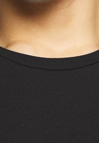 Camiseta de algodón negra con cuello redondo clásico. La tela parece suave y ajustada, mostrando un diseño sencillo y limpio.