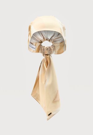 Šviesiai rudos ir kreminės spalvų galvos skara su raukšlėtu elastingu juostos gale ir ilgais, lengvai surištais galais.