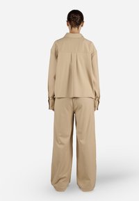 Completo beige in due pezzi che comprende una camicia con colletto dalla vestibilità rilassata e chiusura a bottoni, abbinata a pantaloni a gamba larga, realizzati in un tessuto liscio e con una consistenza morbida.