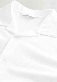 Weißes Poloshirt mit weicher Textur, klassischem Kragen und Knopfverschluss. Hergestellt aus Baumwolle mit glatter Oberfläche und einfachem Design.