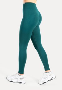 Turkooizen leggings met hoge taille en een gestructureerd patroon, voorzien van een aansluitend ontwerp en een gladde afwerking, gecombineerd met witte sportschoenen.